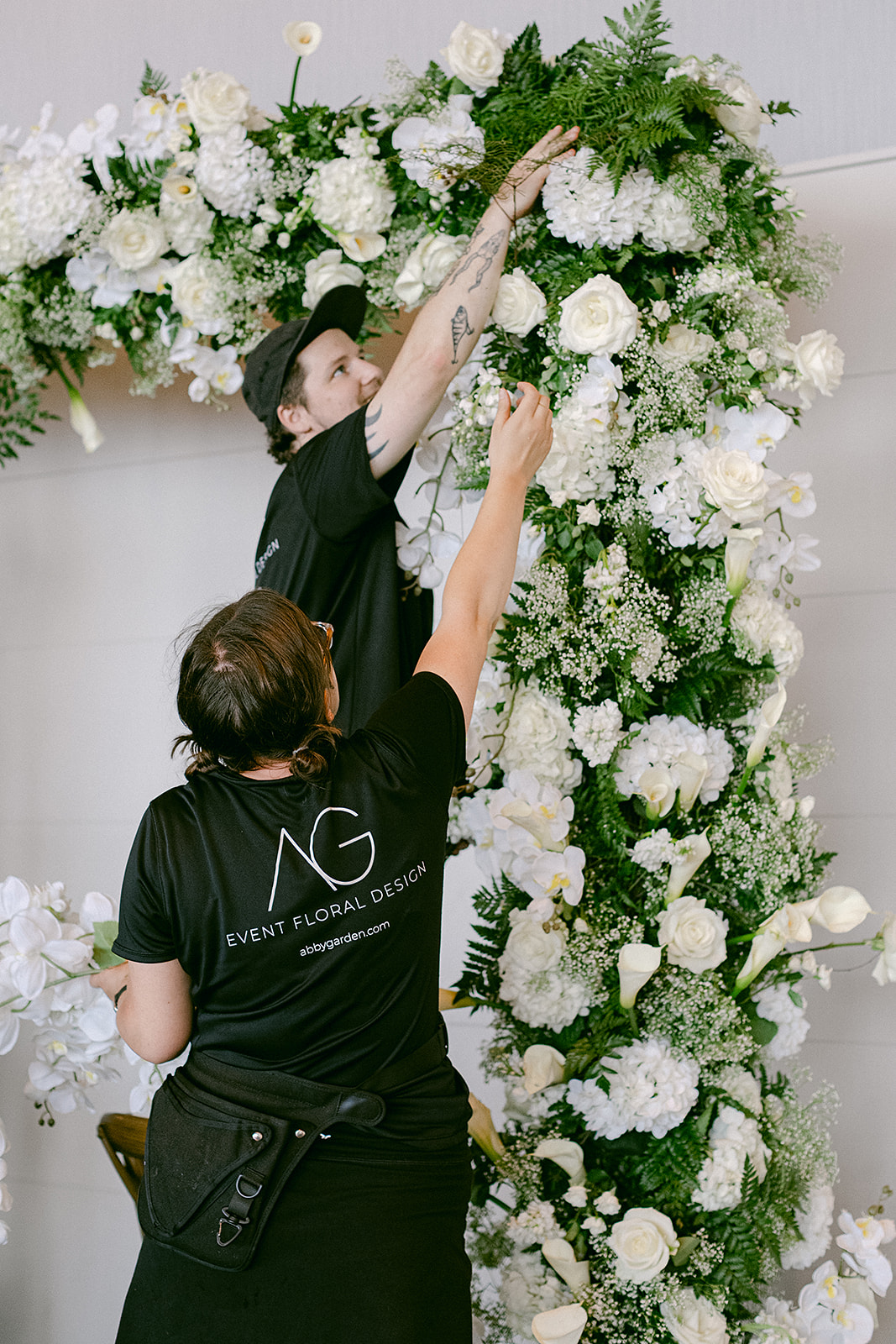 Two florists put together a large floral arch at a wedding
