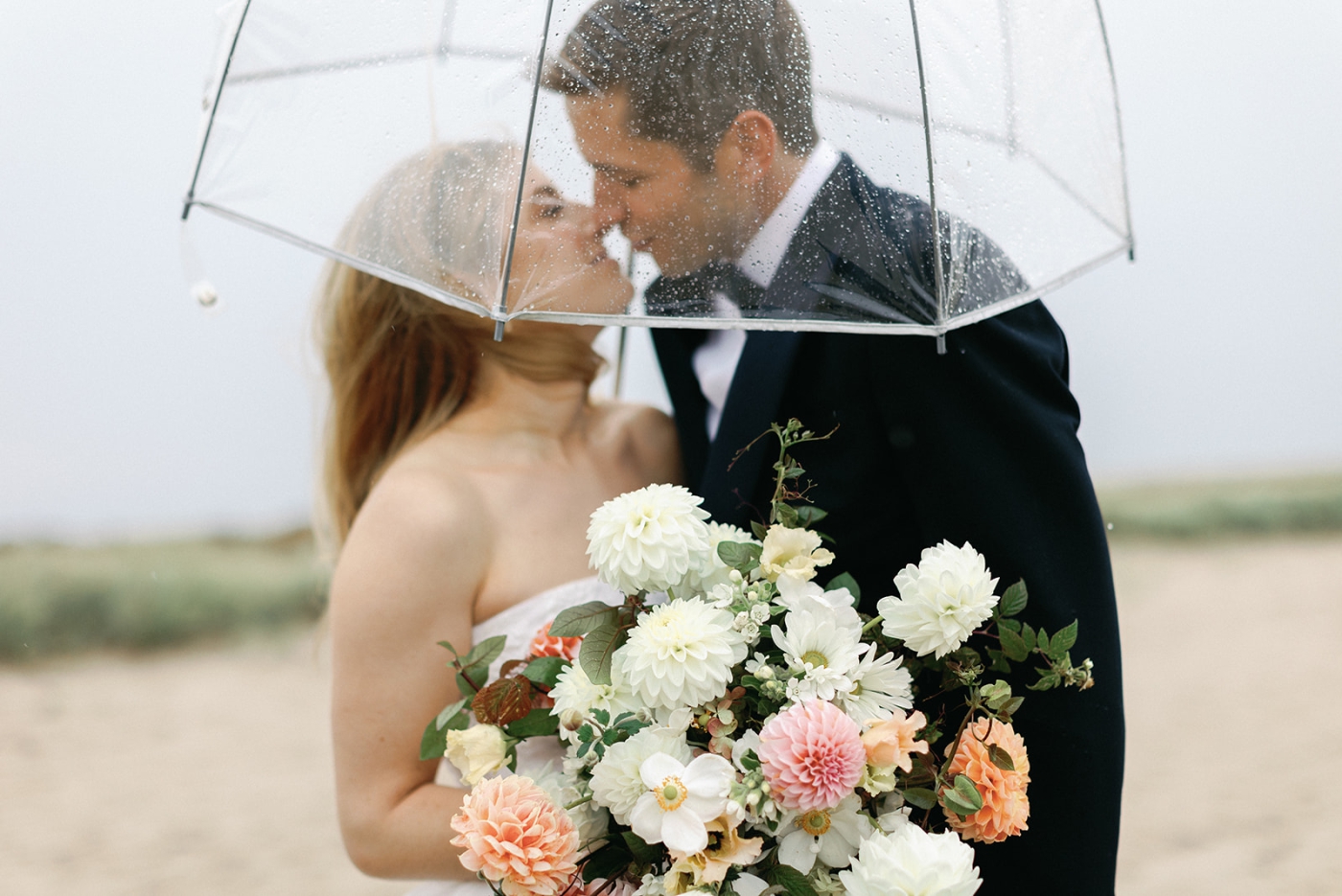 A bride and groom on the beach at Kalmar Village beneath a clear umbrella on a rainy day 