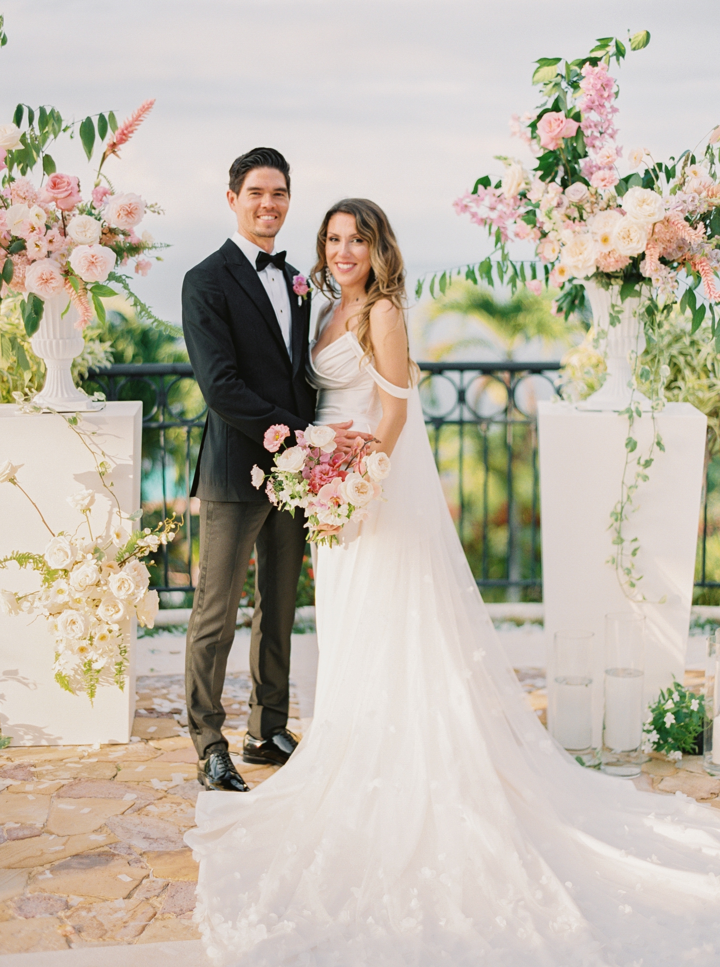 A bride and groom stand at the altar with floral arrangements on pillars flanking them