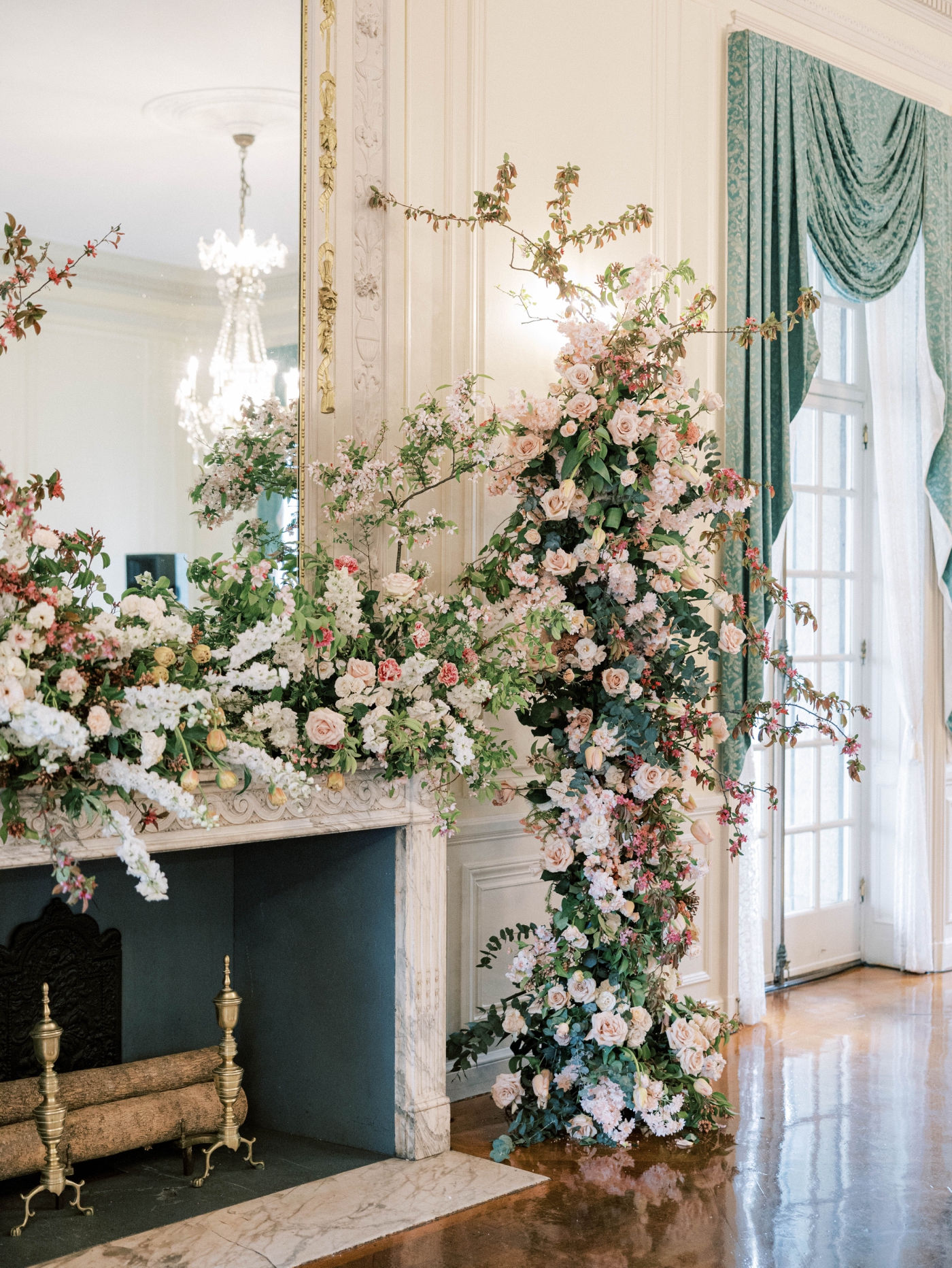 A fireplace decorate with white and pink flowers and cascading greenery