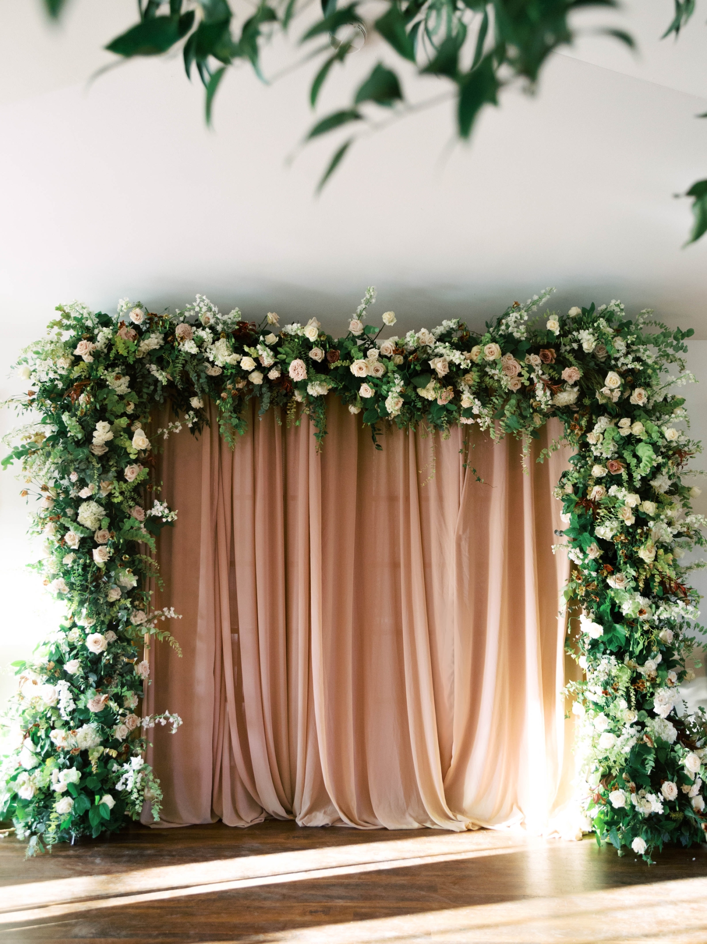 A ceremony altar arrangement with fabric draping from an arbor covered in white and pastel flowers