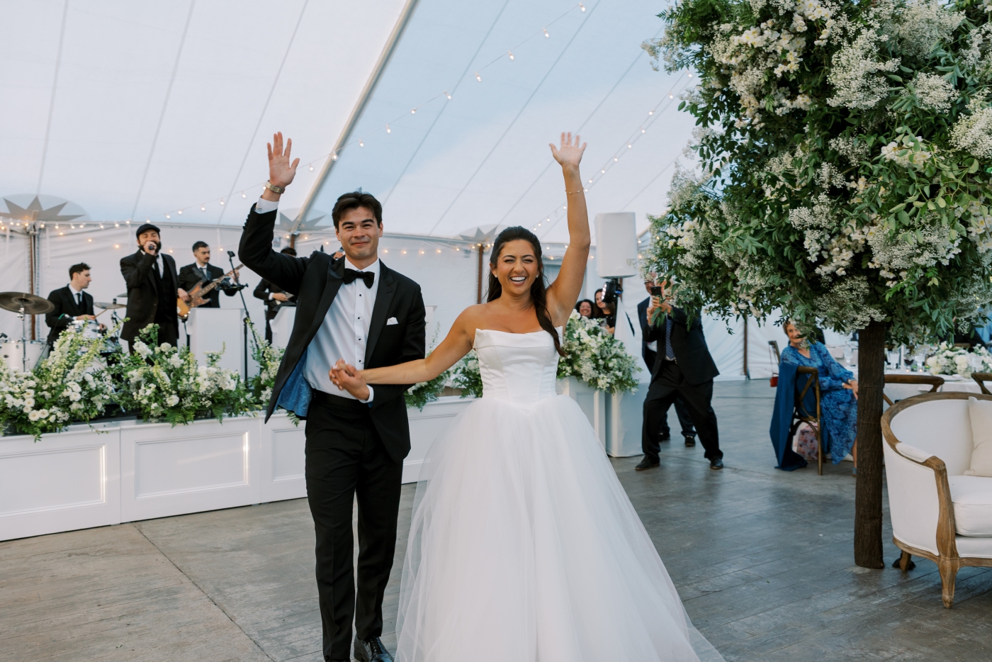 A bride and groom enter their wedding reception while a live band plays on stage 